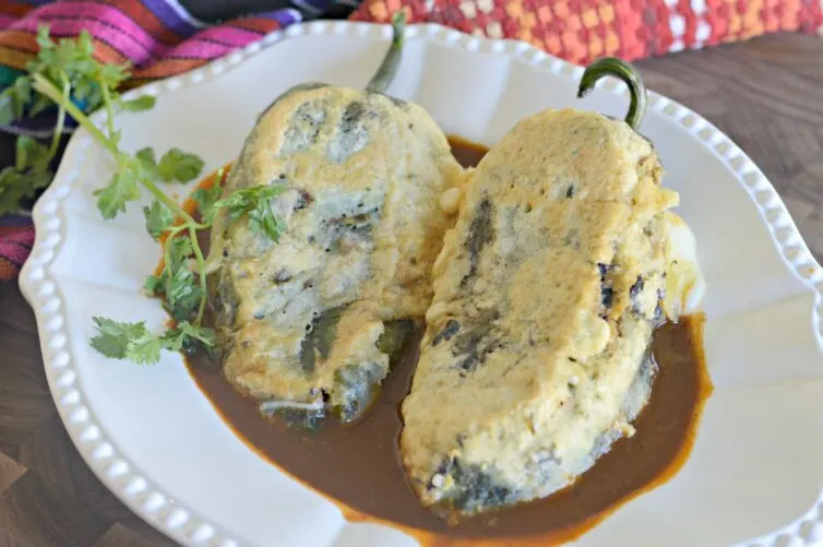 Chiles rellenos de queso on a white plate with an ancho chile salsa garnished with cilantro