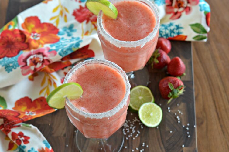 two strawberry margarita mocktails with lime wedges and strawberries next to them