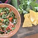 Pico de gallo in a brown bowl on a table with chips next to them