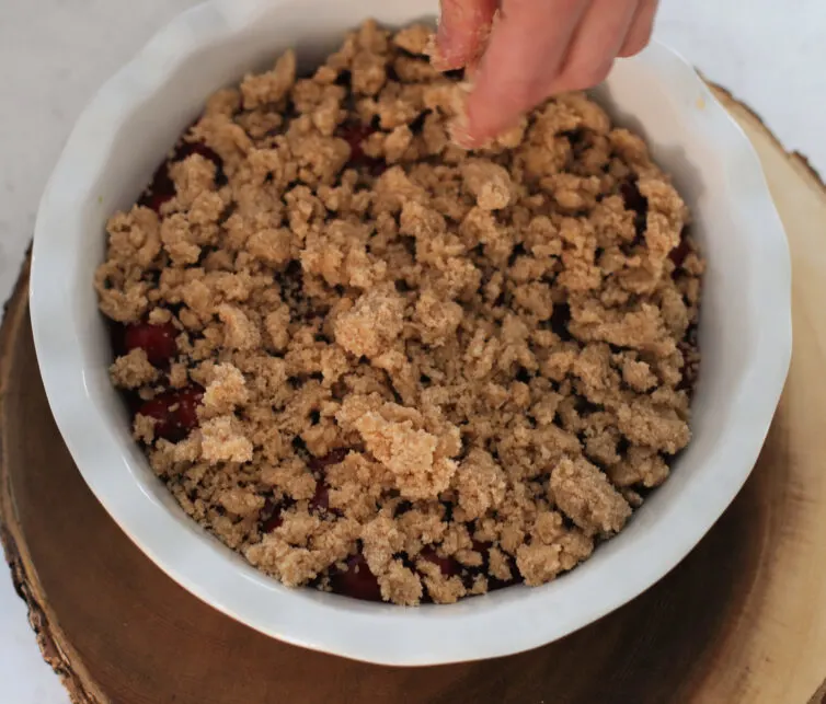 Adding the crumble to the cherry cobbler before baking it