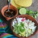 Pozole blanco in a brown bowl with hot salsa and tostadas