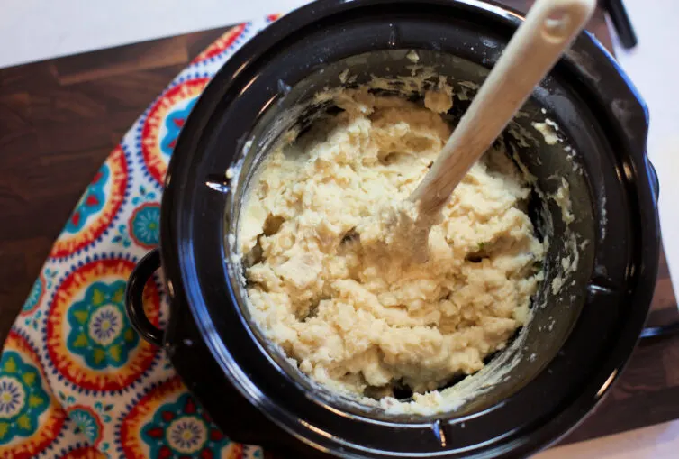 Mashed potatoes in a crockpot with a wooden spoon