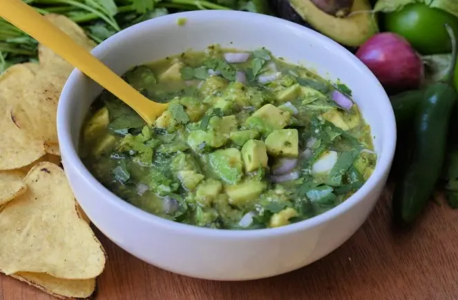 avocado salsa verde with a yellow spoon and fresh ingredients