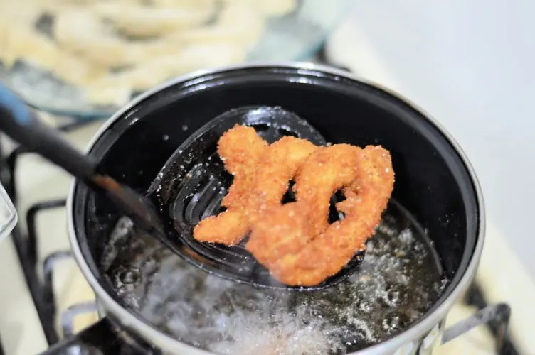 four pieces of shrimp being fried in a deep pot of hot oil