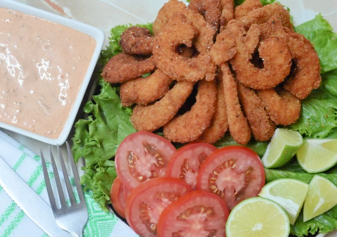 recently cooked fried shrimp on a plate with garnishes such as tomatoes, lime wedges and creamy sauce