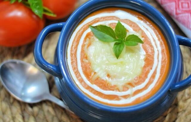 tomato soup in a blue bowl with a spoon and vine ripened tomatoes next to it