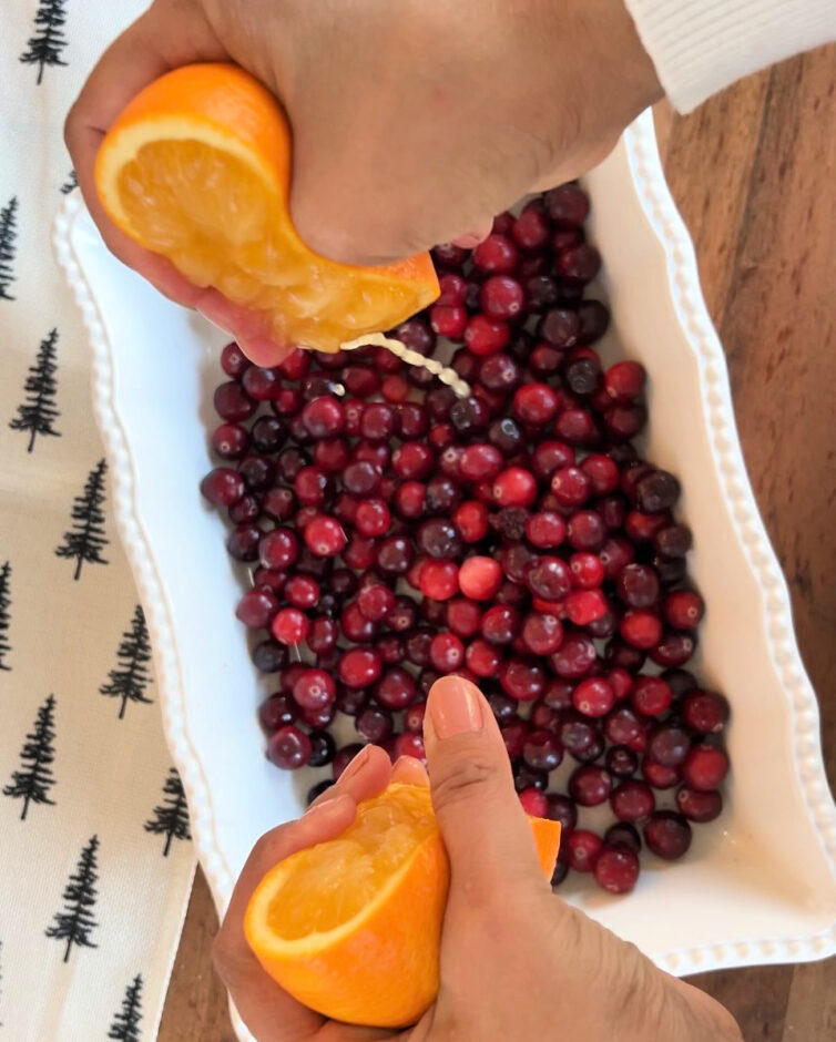 Cranberries in a baking dish with a person squeezing orange juice into it