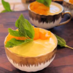 mango mousse in a cute gold and white bowl with a mint leaf on top