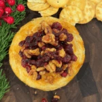 Brie horneado con galletas saladas sobre una mesa de madera, decorado con ar&aacute;ndanos.