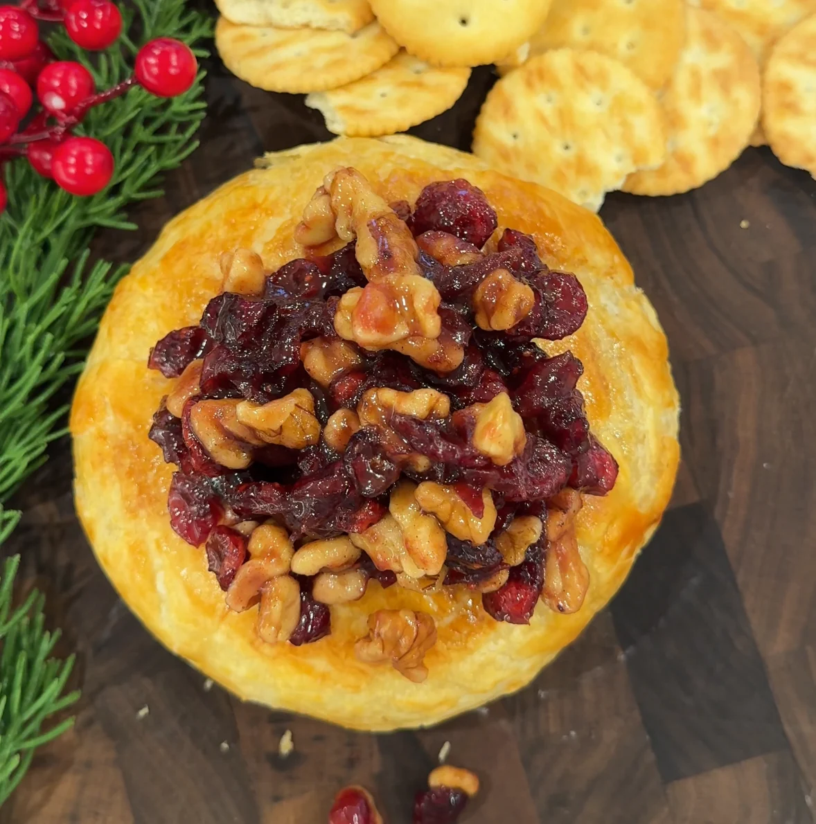 Brie horneado con galletas saladas sobre una mesa de madera, decorado con ar&aacute;ndanos.