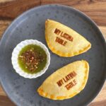 baked empanadas on a gray plate with chimichurri next to it